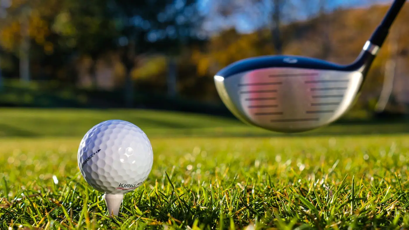 A golf ball on a tee with a driver on a sunny course